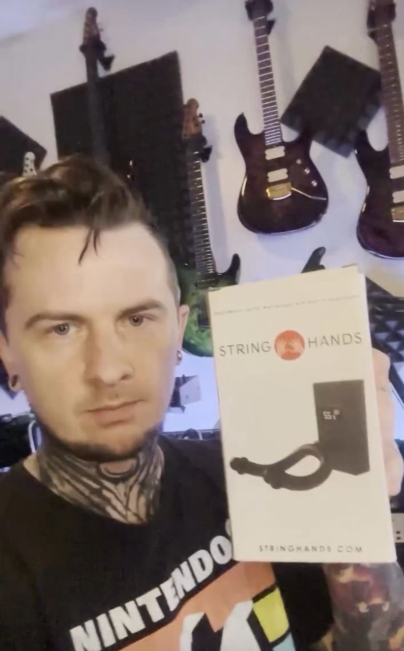 Jason Richardson holding the StringHands HygroMount box in front of his wall of guitars.